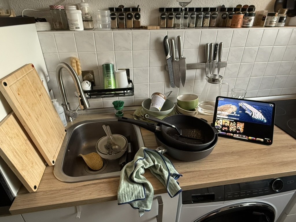 Volle Spüle mit Geschirr, daneben läuft auf einem Tablet ein Video.