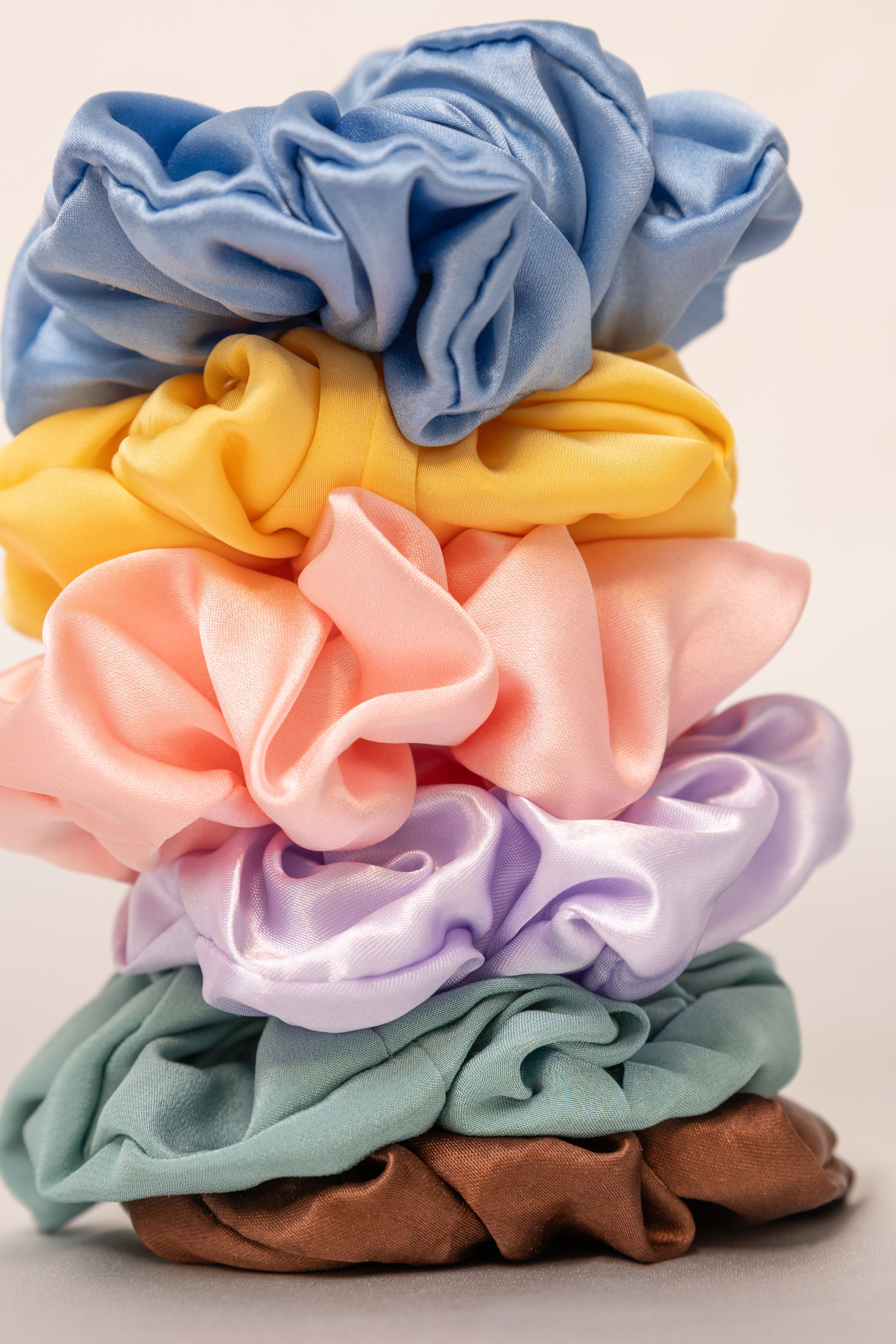 Ein Stapel dicker Stoff-Scrunchies in verschiedenen Farben, die sicherere Alternative zu dünnen Haargummis.
