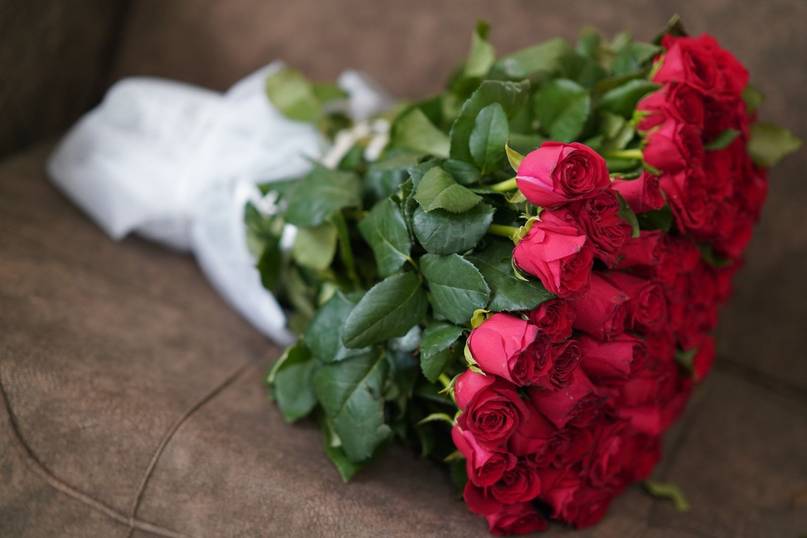 Strauß roter und rosa Rosen in einer Glasvase auf einem hellen Holztisch.